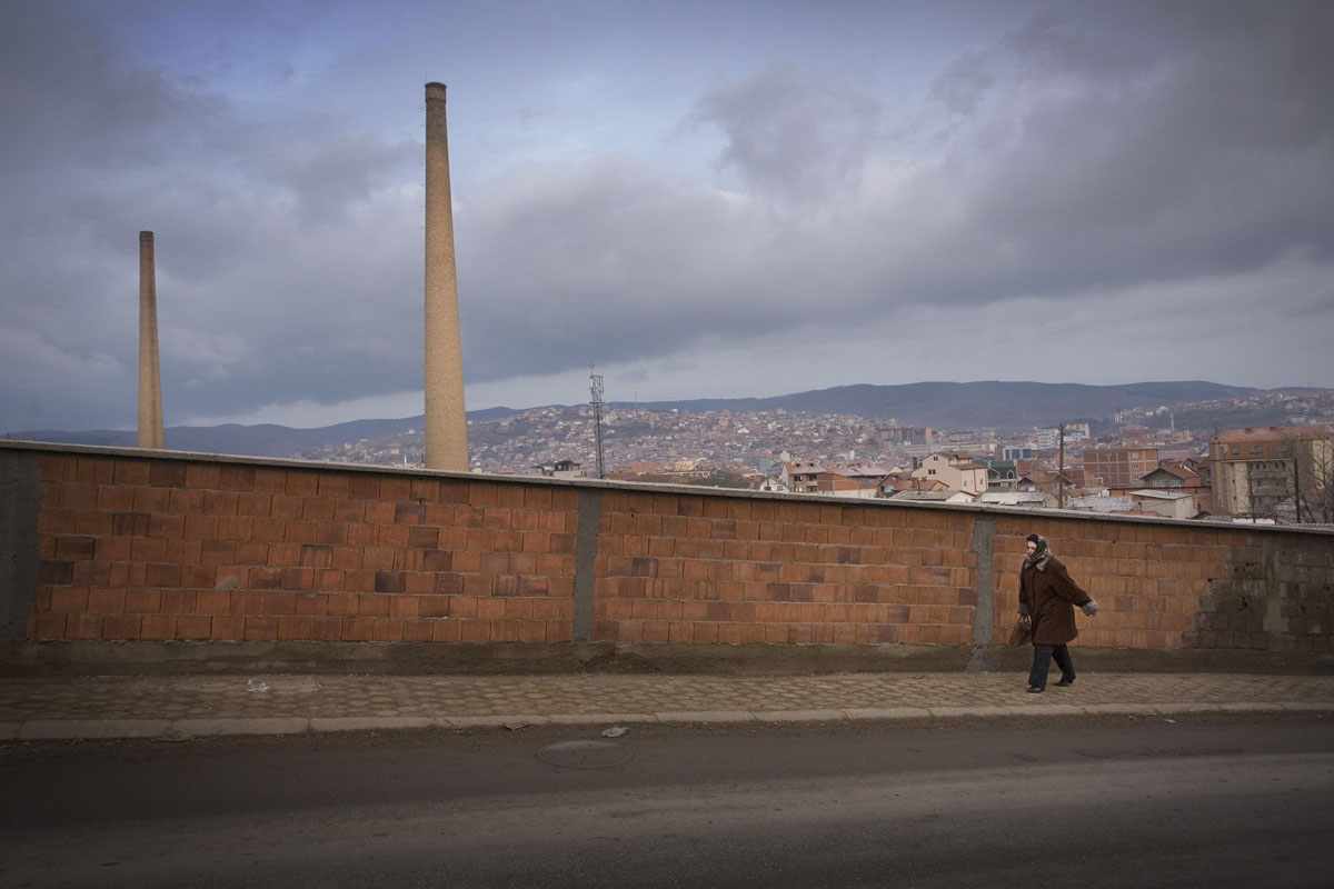 A woman passes the old factories in Pristina, where unemployment is at a staggering height.